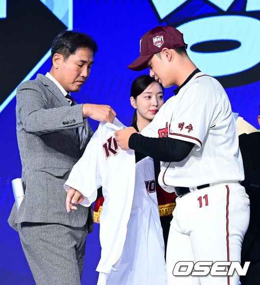 [OSEN=지형준 기자] 11일 오후 서울 잠실 롯데호텔 월드에서 2025 KBO 신인 드래프트가 열렸다.2025 KBO 신인 드래프트는 전면 드래프트 방식으로 진행된다. 지명은 1라운드부터 11라운드까지 이뤄지며, 2023년도 구단 순위의 역순인 키움-한화-삼성-롯데-KIA-두산-NC-SSG-KT-LG 순서로 실시된다.덕수고 정현우가 전체 1순위로 키움에 지명되며 고형욱 단장에게 유니폼을 건네받고 있다. 2024.09.11 /