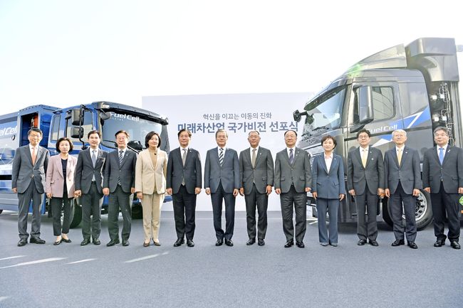 앞 줄 왼쪽 네 번 째 부터 이재명 경기도지사, 박영선 중소벤처기업부 장관, 성윤모 산업통상자원부 장관, 문재인 대통령, 정의선 현대차그룹 수석부회장, 홍남기 경제부총리 겸 기획재정부 장관, 김현미 국토교통부 장관 등이 수출형 수소전기트럭 및 수소전기청소트럭을 배경으로 기념촬영을 하고 있다.