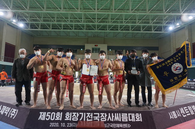 26일 경상남도 고성군 고성군국민체육센터에서 열린 ‘제50회 회장기전국장사씨름대회’ 대학교부 단체전 결승에서 우승한 경남대학교가 노명식 코치(오른쪽 첫 번째-상패), 모제욱 감독(오른쪽 두 번째)과 황경수 대한씨름협회 회장 직무대행(왼쪽)과 함께 기념촬영을 하고 있다.ⓒ 대한씨름협회
