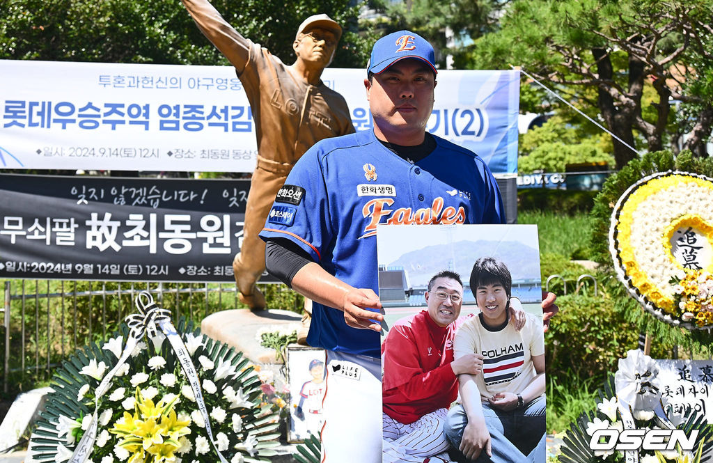 투혼, 헌신, 희생, 도전의 아이콘 불멸의 무쇠팔 故 최동원 감독 13주기 추모행사가 14일 부산 사직야구장 최동원 동상 앞에서 열렸다.1984 한국시리즈에서 혼자 4승을 따내 팀을 창단 첫 우승으로 이끌며 롯데 자이언츠 최초 영구 결번(11번)으로 지정된 선수이다.한화 류현진이 故 최동원 감독 동상 앞에서 헌화를 마치고 신인시절 최동원 감독과 함께 찍은 사진을 들고 기념촬영을 하고 있다. 2024.09.14 / foto0307@osen.co.kr