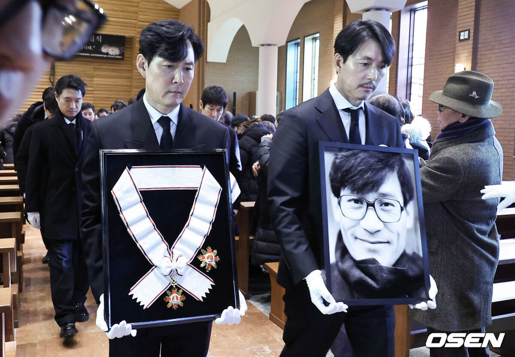 [OSEN=사진팀] 故 안성기 장례 미사 및 영결식이 9일 서울 명동성당에서 엄수됐다.안성기는 지난 5일 오전 9시 서울 용산구 순천향대병원 중환자실에서 치료를 받던 중 가족들이 지켜보는 가운데 향년 74세로 세상을 떠났다. 지난달 30일 자택에서 음식물이 목에 걸린 채 쓰러져 병원으로 이송된 뒤 의식불명 상태로 치료를 받아온 지 6일 만이다.영결식에서는 고인의 마지막 소속사 아티스트컴퍼니의 수장인 정우성과 이정재가 각각 영정과 훈장을 들며 고인을 배웅했다. 운구는 설경구, 박철민, 유지태, 박해일, 조우진, 주지훈이 맡았다.배우 정우성, 이정재가 영정과 금관문화훈장을 들고 운구 행렬과 영결식장을 나서고 있다. 2026.01.09 / photo@osen.co.kr사진=사진공동취재단