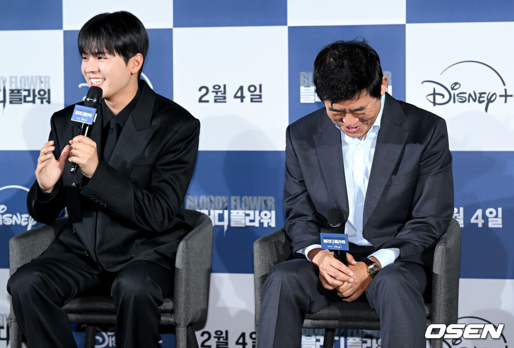 디즈니+ '블러디 플라워' 제작발표회가 27일 서울 용산구 CGV용산아이파크몰에서 열렸다.블러디 플라워‘는 모든 불치병을 치료할 수 있는 능력을 가진 연쇄살인범을 둘러싼 사람들의 이야기를 그린 미스터리 스릴러다. 배우 성동일이 려운의 인터뷰 답변에 미소를 짓고 있다. 2026.01.27 /cej@osen.co.kr