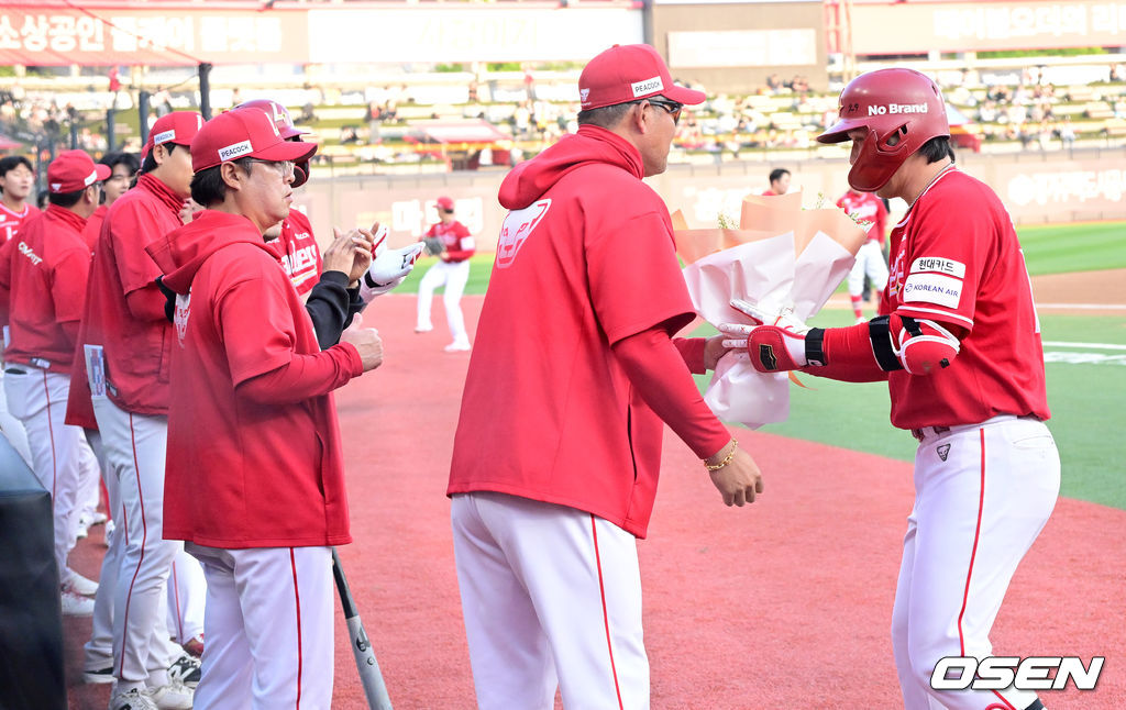 꽃다발을 건네며 최정의 대기록을 축하하는 SSG 이숭용 감독과 더그아웃 앞 도열해 박수를 보내는 선수단과 코칭스태프.