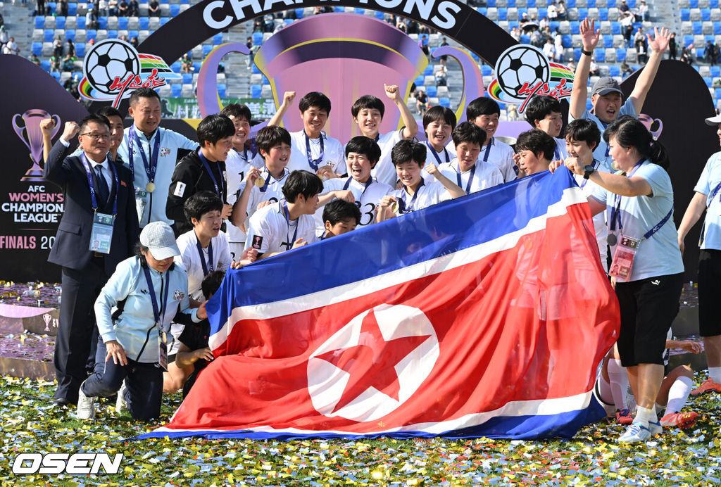 우승컵도, 100만 달러(약 15억 원) 우승 상금도 북한 내고향여자축구단 차지가 됐다. 논란 속 한국에서 열린 결승전에서 내고향은 일본 도쿄 베르디 벨레자를 꺾고 아시아 정상에 올랐다. 경기장 분위기 역시 마지막까지 씁쓸함을 남겼다.내고향은 23일 오후 수원종합운동장에서 열린 2025-2026 아시아축구연맹(AFC) 여자 챔피언스리그(AWCL) 결승전에서 도쿄 베르디를 1-0으로 꺾고 우승을 차지했다. 이날 공식 관중은 2670명이었다.경기 종료 후 내고향여자축구단 선수단이 인공기를 펼치고 기념촬영을 하고 있다. 2026.05.23 /sunday@osen.co.kr