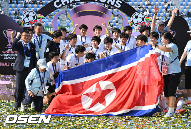[OSEN=수원, 이대선 기자] 우승컵도, 100만 달러(약 15억 원) 우승 상금도 북한 내고향여자축구단 차지가 됐다. 논란 속 한국에서 열린 결승전에서 내고향은 일본 도쿄 베르디 벨레자를 꺾고 아시아 정상에 올랐다. 경기장 분위기 역시 마지막까지 씁쓸함을 남겼다.내고향은 23일 오후 수원종합운동장에서 열린 2025-2026 아시아축구연맹(AFC) 여자 챔피언스리그(AWCL) 결승전에서 도쿄 베르디를 1-0으로 꺾고 우승을 차지했다. 이날 공식 관중은 2670명이었다.경기 종료 후 내고향여자축구단 선수단이 인공기를 펼치고 기념촬영을 하고 있다. 2026.05.23 /sunday@osen.co.kr