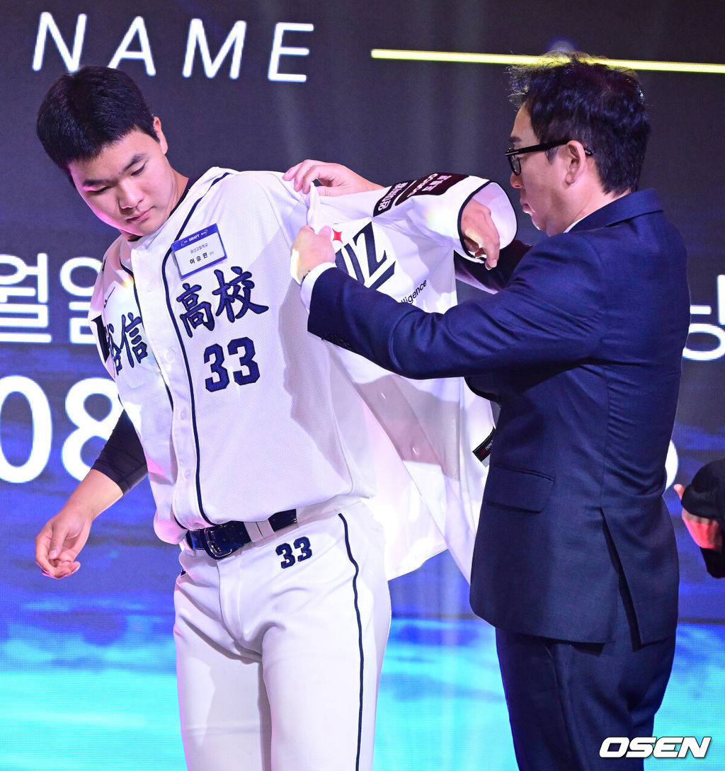 21일 오후 서울 잠실동 롯데호텔 월드 크리스탈볼룸에서 ‘2027 KBO 신인드래프트’가 열렸다. 이번 신인드래프트는 2025시즌 순위의 역순에 따라 키움 히어로즈, 두산 베어스, KIA 타이거즈, 롯데 자이언츠, KT 위즈, NC 다이노스, 삼성 라이온즈, SSG 랜더스, 한화 이글스, LG 트윈스 순서로 1라운드부터 11라운드까지 지명할 수 있다. 유신고 이승원이 KT 1라운드에 지명된 뒤 나도현 단장에게 유니폼을 전달받고 있다. 2026.09.21 / dreamer@osen.co.kr