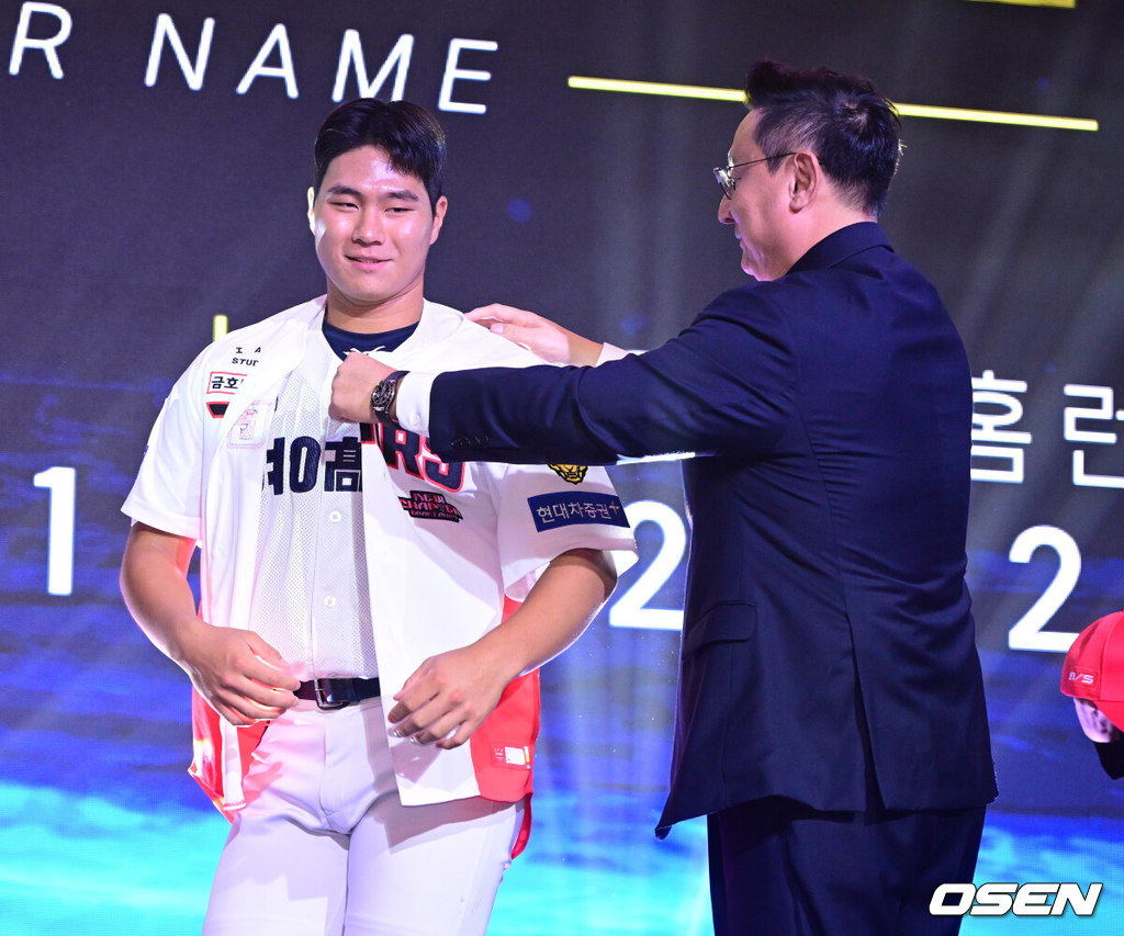 21일 오후 서울 잠실동 롯데호텔 월드 크리스탈볼룸에서 ‘2027 KBO 신인드래프트’가 열렸다. 이번 신인드래프트는 2025시즌 순위의 역순에 따라 키움 히어로즈, 두산 베어스, KIA 타이거즈, 롯데 자이언츠, KT 위즈, NC 다이노스, 삼성 라이온즈, SSG 랜더스, 한화 이글스, LG 트윈스 순서로 1라운드부터 11라운드까지 지명할 수 있다. 경남고 이호민이 전체 3번으로 KIA 타이거즈에 지명된 뒤 심재학 단장에게 유니폼을 전달받고 있다. 2026.09.21 / dreamer@osen.co.kr